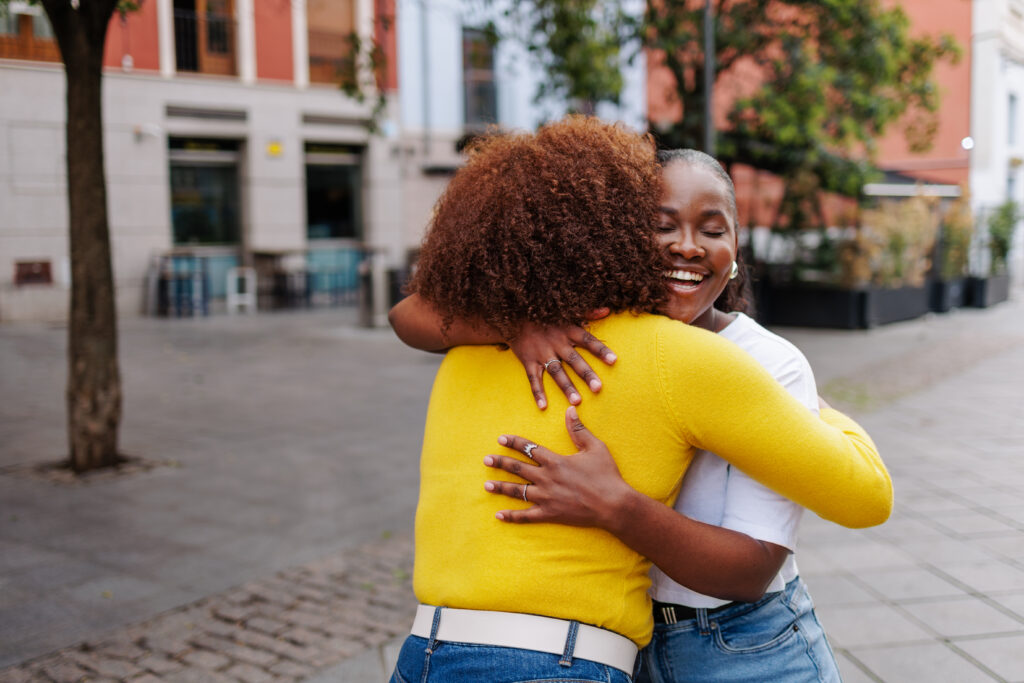black gen z woman hugging friend in city street. female friends meeting. copy space.