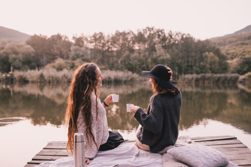 two women friends having picnic in autumn forest near lake.