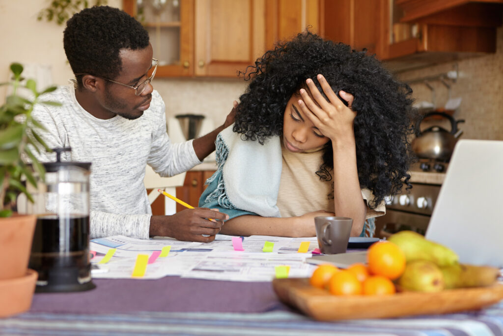 young dark skinned woman feeling stressed, holding head in despair, can't stand through financial trouble while man in spectacles trying to calm her down, telling that everything will be alright